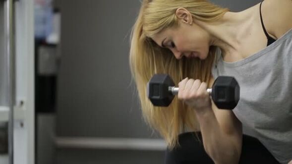 The girl performs a dumbbell exercise